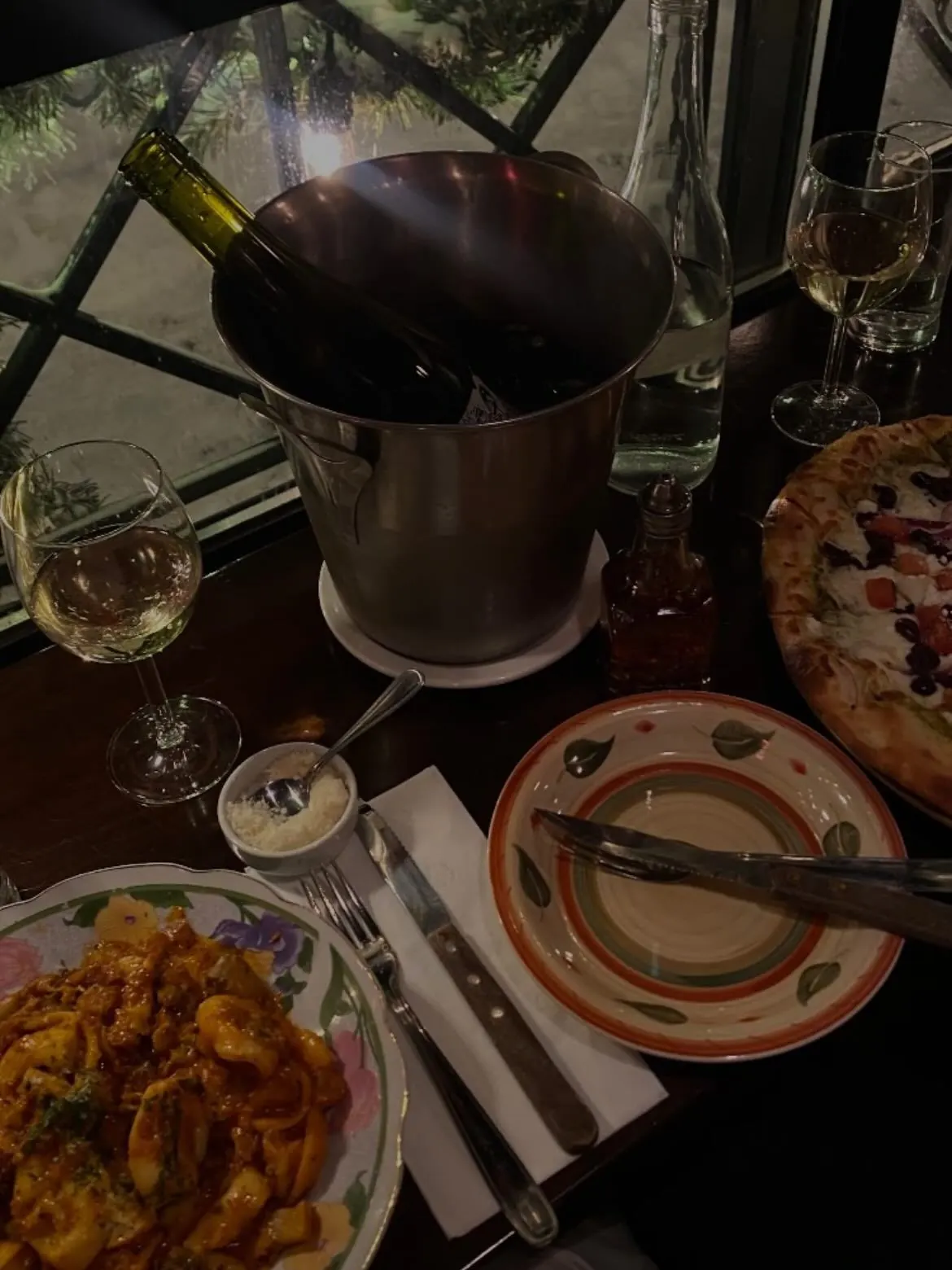 A wine bottle in a bucket, glasses and pizza on the table